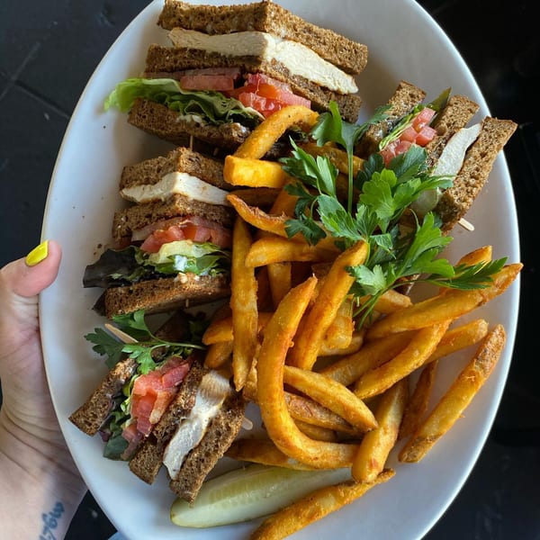 A diner-style chicken club sandwich with fries and a pickle spear on a white plate.