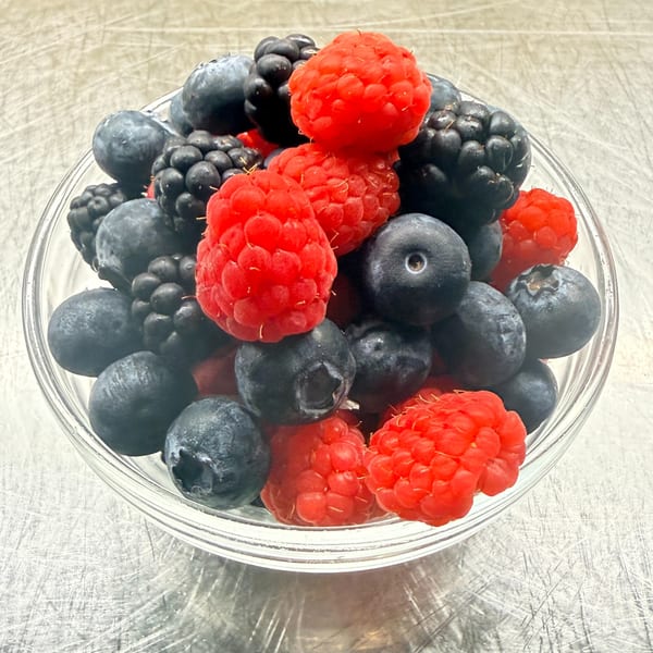A clear glass bowl filled with fresh, vibrant blueberries, raspberries, and blackberries.