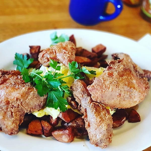 Fried chicken and home fries with scrambled eggs and parsley on a white plate.