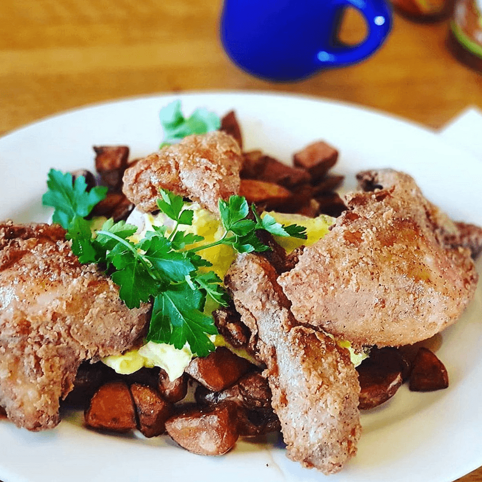 Fried chicken and home fries with scrambled eggs and parsley on a white plate.