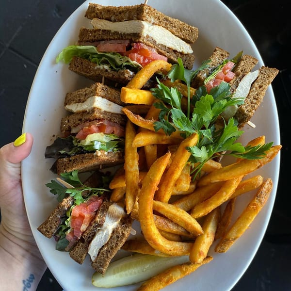 The Kettle's chicken club sandwich with lettuce, tomato, and fries, garnished with parsley and a pickle.