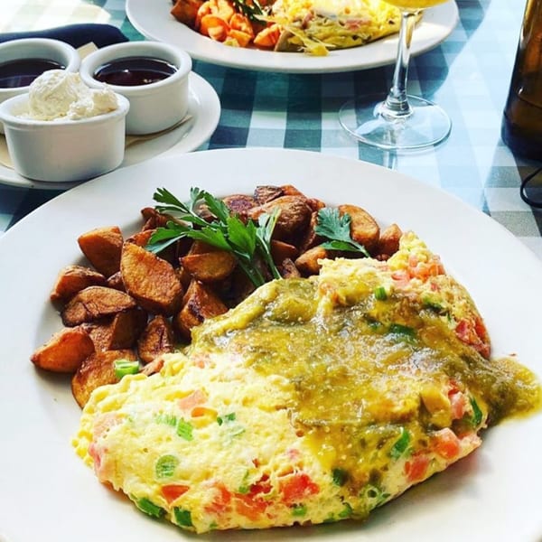 A diner breakfast of omelet with green salsa, home fries, and sides on a checkered tablecloth.