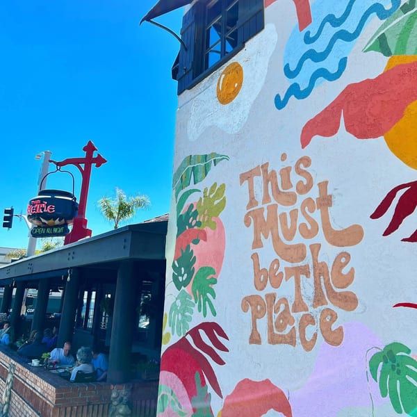 The Kettle diner's exterior with a colorful mural and outdoor patio seating under a blue sky.
