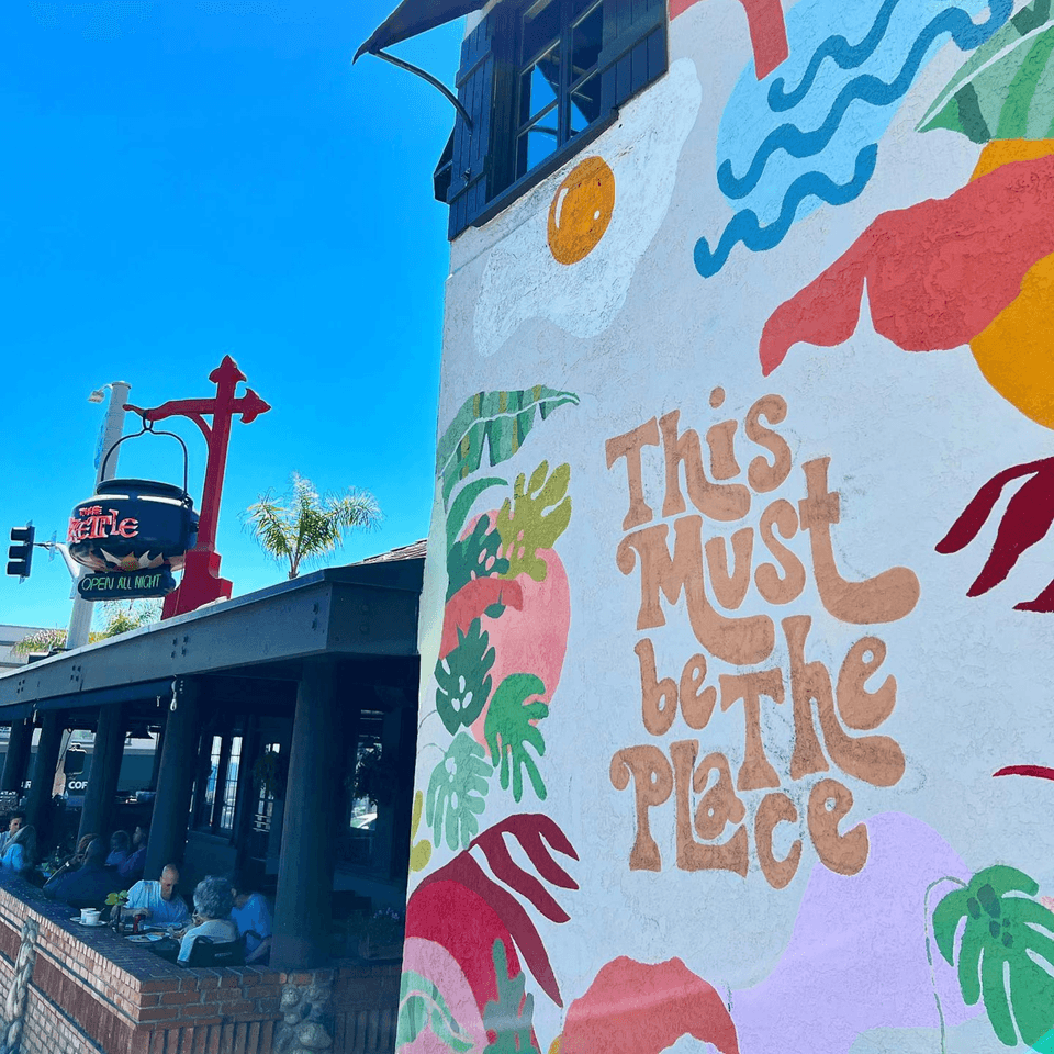 The Kettle diner's exterior with a colorful mural and outdoor patio seating under a blue sky.