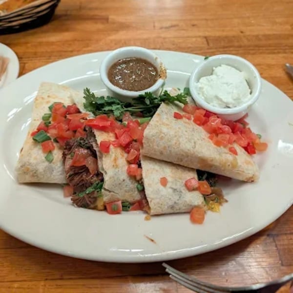 Shredded beef quesadillas topped with diced tomatoes and green onions, served with refried beans and sour cream.