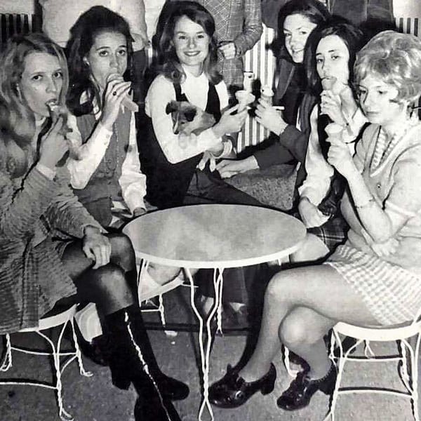 Six young women in 1960s attire enjoy ice cream cones around a small table at The Kettle diner.