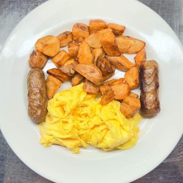 A white plate holds a breakfast of scrambled eggs, two sausage links, and roasted potatoes.