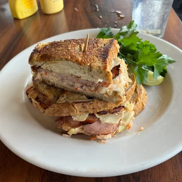 A stacked deli sandwich with toasted bread, meat, and coleslaw, garnished with parsley and lime.