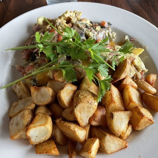 A diner breakfast plate with scrambled eggs, home fries, and fresh parsley on a white plate.