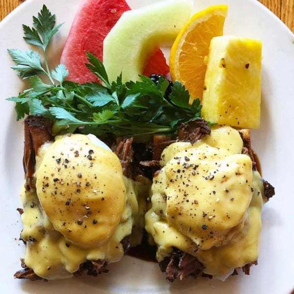 Eggs Benedict with hollandaise sauce and black pepper, served with a side of fresh fruit.